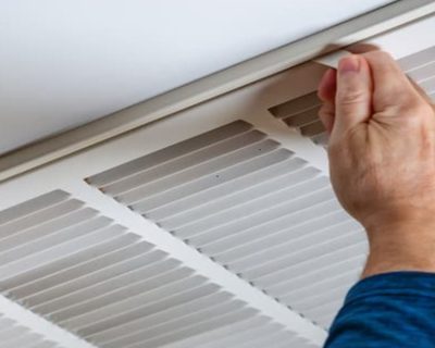 Technician opening ceiling air duct vent cover for professional cleaning inspection